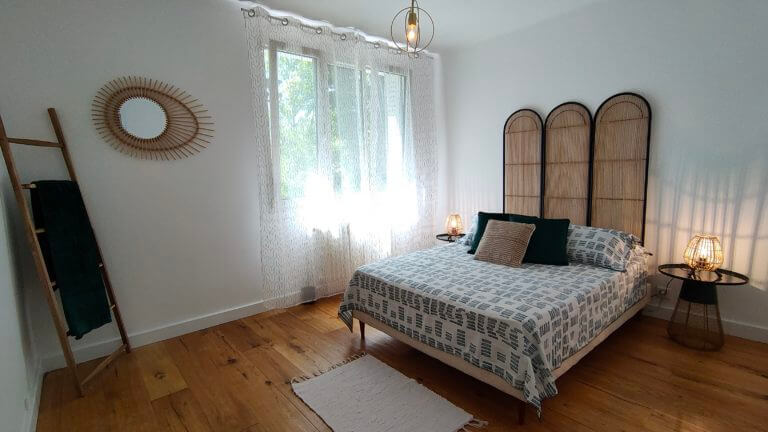 Une chambre avec un lit double, un paravent tressé en tête de lit et de la décoration en bois après un home staging
