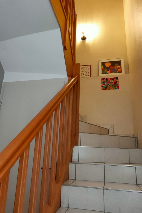 home-staging-descente-escalier-avant Une montée d'escalier avec des marches en carrelage blanc, une rampe couleur chêne et des murs jaunes clairs avant un home staging