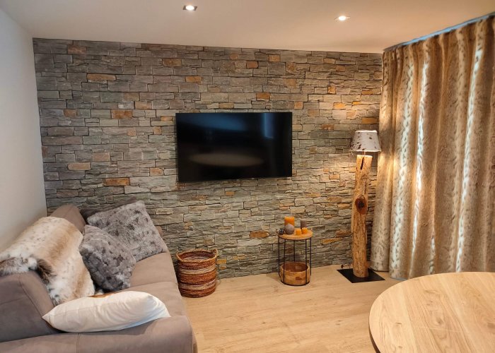 home-staging-salon-apres Le salon d'un meublé touristique dans les tons lin et taupe avec un canapé, un lampadaire et un mur en parements après un home staging